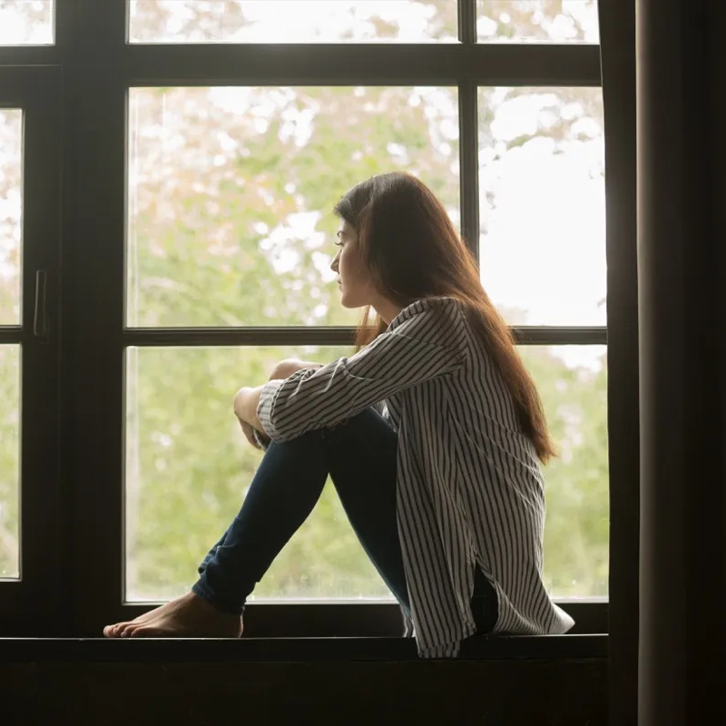 Jeune fille mélancolique assise à sa fenêtre et qui regarde dehors